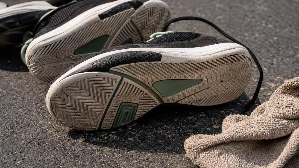 Close-up of unbranded basketball shoe outsoles on rough blacktop showing dusty tread for outdoor durability checks