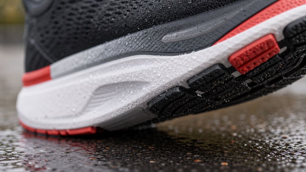 Generic running shoe outsole and midsole close-up on wet pavement showing traction texture, foam layers, and water beads